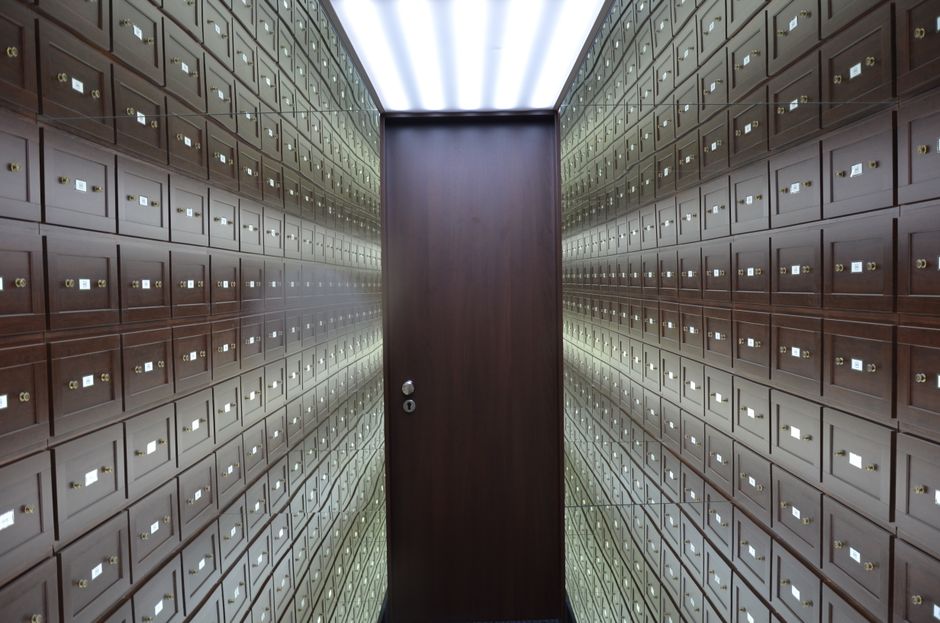 Wooden lockboxes line the walls of a modern, secure vault with a central wooden door.